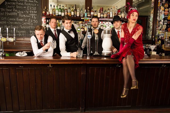 Band members dressed in vintage clothes behind a pub bar